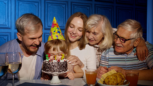 家人聚会摄影照片_可爱的小女孩吃蛋糕许愿，玩得开心，与家人一起庆祝生日聚会