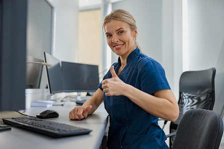 现代诊所接待台的值班护士在电脑上工作并竖起大拇指