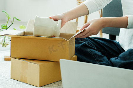 亚洲女店主折叠产品并包装在纸板包裹箱中。