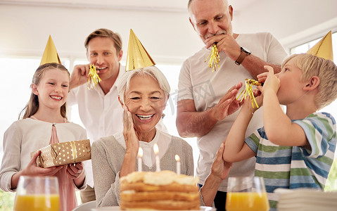 高级妇女在家里与家人一起庆祝生日，戴着派对帽，吹着口哨。