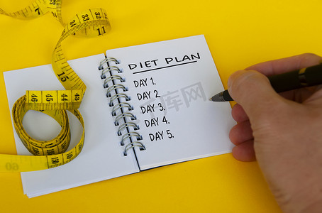 白色记事本上的饮食计划文本，黄色背景上有卷尺。