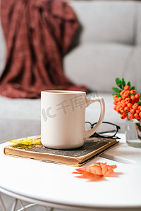 客厅桌子摄影照片_静物书、蜡烛、罗文浆果和一杯茶或咖啡在客厅的桌子上，家居装饰在舒适的房子里。