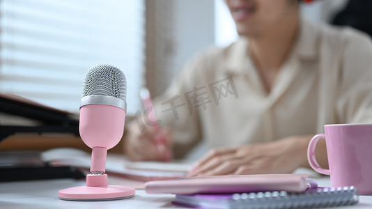 职业粉色摄影照片_白桌上有一个粉色麦克风，微笑的男播客在舒适的家庭工作室里播放着他的音频播客