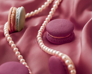 丝绸背景上的甜马卡龙和珍珠首饰、巴黎别致珠宝、法式甜点食品和豪华糖果品牌的蛋糕马卡龙、节日礼物