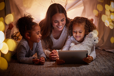 晚上，母亲和孩子们在家里的帐篷里露营，使用平板电脑在应用程序上进行直播。