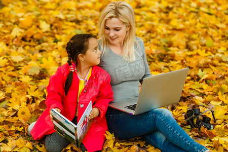 秋季公园里，快乐微笑的母子坐在一起看书或平板电脑