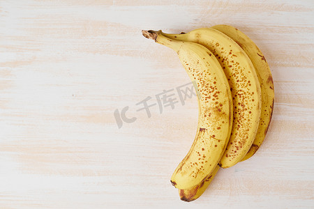 明亮的白色木桌上有棕色斑点的成熟香蕉、复制空间、顶视图