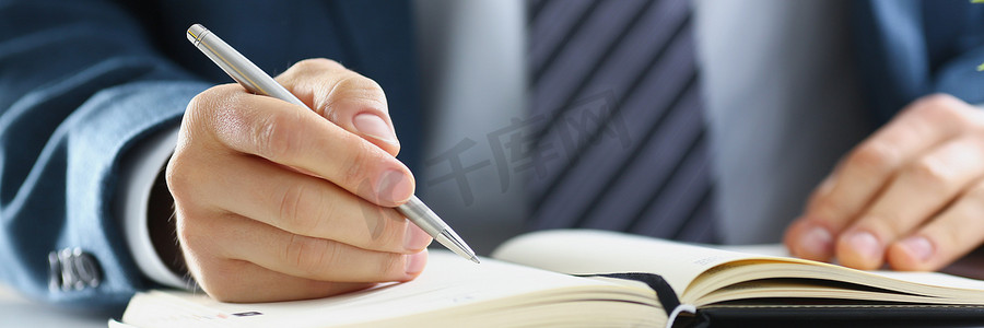 一个穿西装的男人在笔记本上写字，手特写