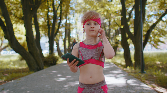 运动健身运动员小女孩行走，使用智能手机带耳机听音乐