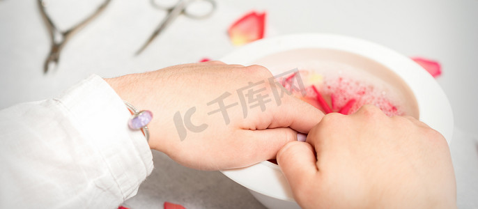 白碗里的手用水和玫瑰花瓣沐浴指甲，以软化角质层和干燥的皮肤。