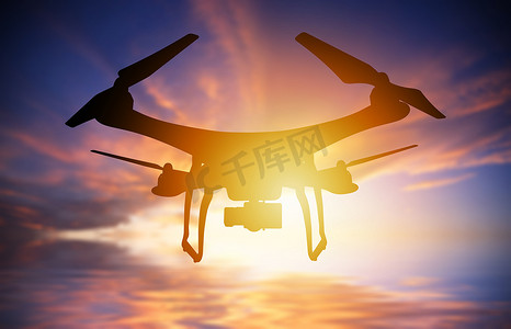 带有数码相机的无人机在夕阳天空中飞行的剪影