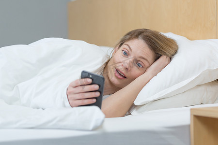 十里红妆摄影照片_躺在床上的毯子下的女人震惊了，微笑着从电话里读到好消息