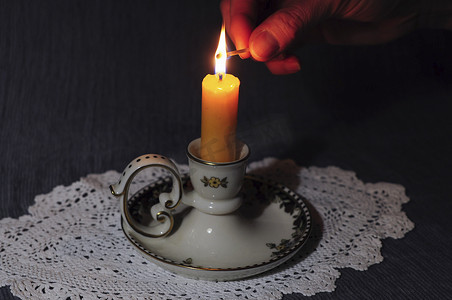 一只手在黑暗中点燃陶瓷烛台上的黄色蜡烛