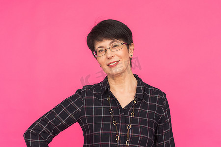 时尚与人物观念 — 戴眼镜、短发的中年女性站在粉色背景上微笑