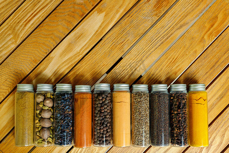 透明罐子里的不同多色印度香料位于木质背景上，有复制空间