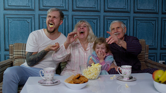看电视卡通摄影照片_多代幸福的家庭笑，看卡通电视电影，在家吃爆米花