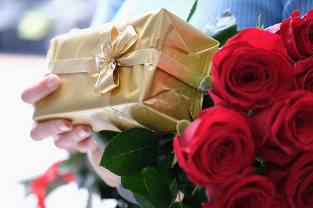 女性手中的红玫瑰花束和金色礼盒