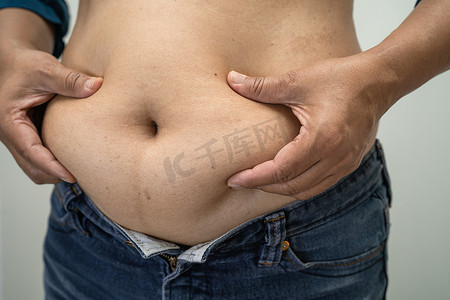 超重的亚洲女性在办公室展示肥胖的腹部。
