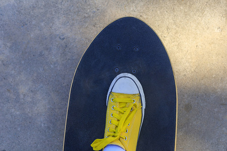早上在公园踩冲浪滑板的黄色运动鞋的特写顶视图。