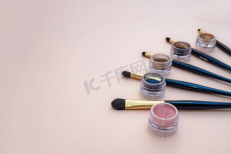 与装饰化妆产品金色刷子和彩色眼影在柔和的粉红色背景上的组合。