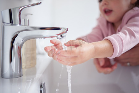 环境卫生治理摄影照片_手、水和清洁，一个女孩和她的母亲在家里的新冠病毒期间在水龙头下洗手，以确保卫生和环境卫生。