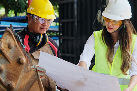 亚洲工程经理和机械工人戴着头盔工作，同时讨论和检查工厂的制造过程。