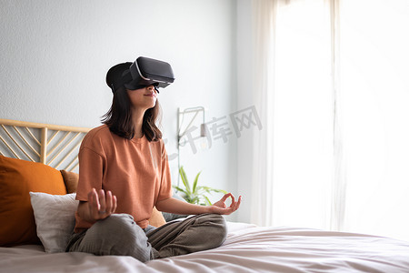 亚洲女性在床上用 VR 体验应用程序冥想。