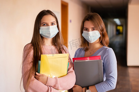 两名戴着医用口罩和学习材料的女学生的肖像