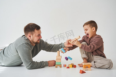 大白爸爸摄影照片_爸爸和儿子微笑着，玩得很开心，在白色背景上玩彩色砖玩具。