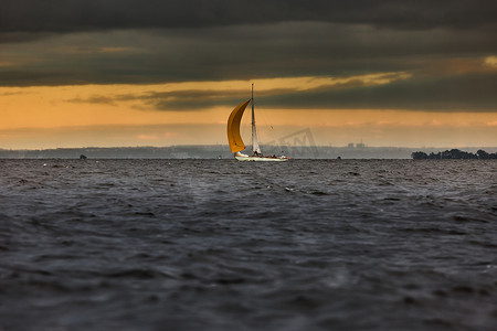 帆船在海上暴风雨天气，风雨如磐的云天橙色天空，风帆赛船会，风帆在水中的反射，大水波，