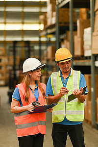 戴着安全帽和背心的仓库工作人员站在摆满货架的零售仓库之间，在平板电脑上查找订单详细信息