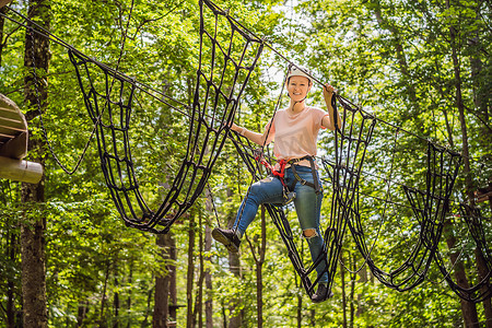 快乐的女女孩在森林中的极限公路电车滑索中滑翔攀爬，在树上的登山扣安全链接上到树顶绳索冒险公园。