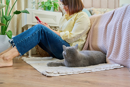 地毯猫摄影照片_女性坐在地板上使用智能手机，宠物猫睡在主人身边