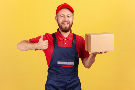 邮政寄递摄影照片_微笑的快递员拿着纸板箱，竖起大拇指，将包裹递送给客户。