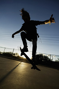 皮包骨摄影照片_日落时的少年滑板运动员
