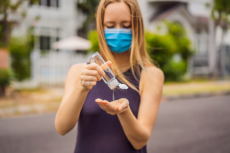 勤洗手小报摄影照片_由于冠状病毒流行，小镇上戴着医用口罩的妇女使用消毒剂