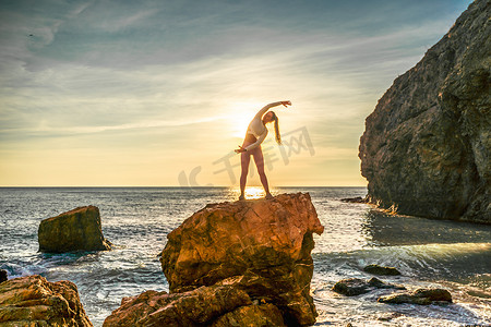 海边女子摄影照片_女子体操运动员正在海边日落的海滩上训练。