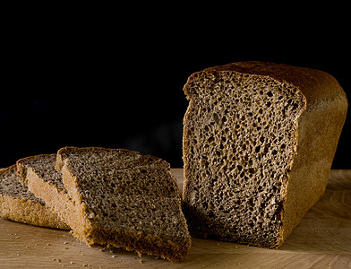 一条黑黑麦面包，切成块，呈黑色背景木板上砖的形状