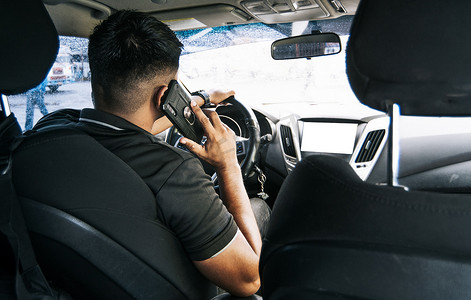 男司机在车里打电话，一个年轻人坐在车里用手机的后视图，男人开车时打电话的概念