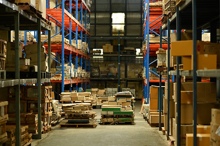大型物流配送仓库内部摆满了货架，货物装在纸板箱和托盘中