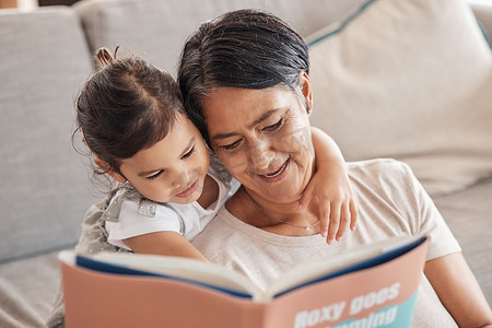 教育、学习和女孩和祖母在沙发上读书，在客厅放松和建立联系。