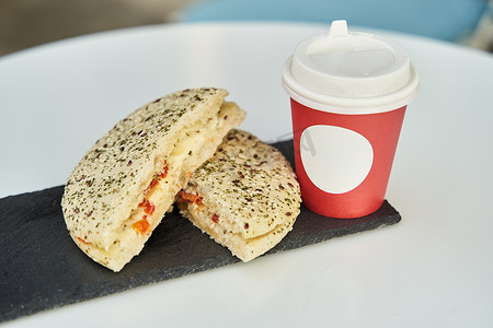 咖啡店的桌子上放着一个三明治，上面放着一杯红色塑料咖啡。