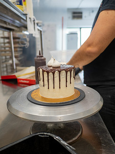 赶车鞭子摄影照片_蛋糕设计师用蛋白酥皮和蓝莓装饰巧克力滴蛋糕