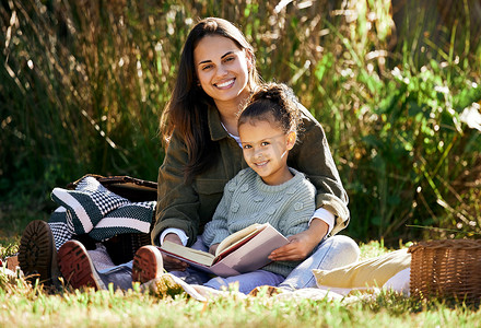 一个小女孩和她的母亲在公园或花园里放松时读书。