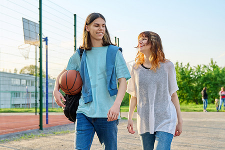 男女学生摄影照片_篮球场附近带球在户外行走的年轻男女学生