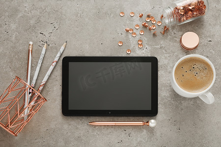 办公桌顶视图，配有空平板电脑、咖啡杯、笔和其他配件。