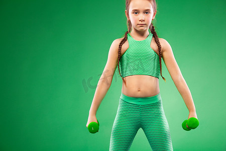 健身的小女孩摄影照片_绿色背景下用哑铃做健身运动的小女孩