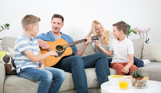 男人唱歌摄影照片_快乐的白人家庭在舒适的现代家里微笑、弹吉他、唱歌