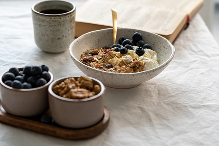 酸奶燕麦摄影照片_看书，吃健康的生活方式早餐，包括麦片麦片和酸奶
