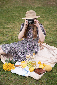 戴草帽的女孩摄影照片_一位穿着长裙、头戴草帽的年轻女子正在野餐时休息，上面有水果